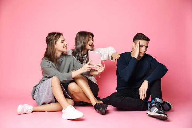 Guy refuse to look in tablet. Friends sitting on pink floor