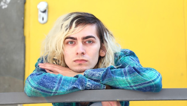 Free photo guy resting his head on his hands on a metal staircase on a yellow door