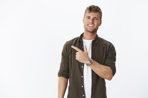 Free photo guy showing us cool place inviting join. friendly-looking sociable and carefree handsome masculine blond man with watch, bristle and blue eyes smiling cute and pointing left with index finger