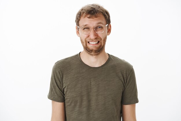Guy squinting and making funny face eating sour lemon frowning and wrinkling nose standing disgusted and dissatisfied in transparent glasses and green t-shirt