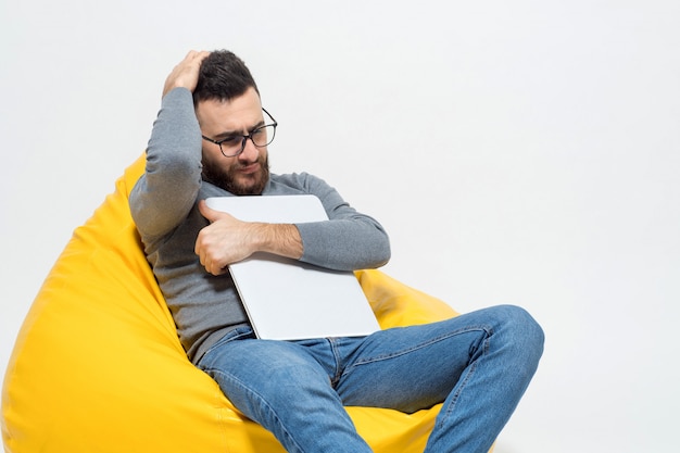 Free photo guy in thoughts while sitting on yellow pouf chair