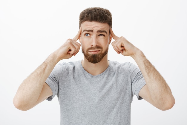 Guy trying focus, think up new plan. Determined, thoughtful handsome charismatic man with beard and blue eyes squinting, smirking holding fingers on temples focusing on importrant game, concentrating