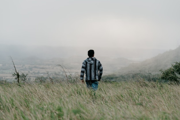 A guy walking in the field through grass on a gloomy foggy day