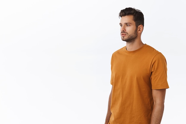 Free photo guy with beard in brown t-shirt, standing half-turned with spaced-out casual expression, looking left, posing white background no emotions