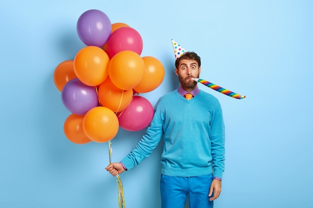 guy with birthday hat and balloons posing in blue sweater