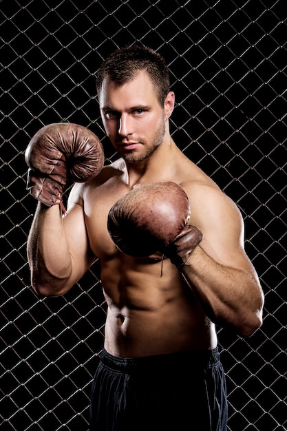 フェンスの上の筋肉を示すボクシンググローブを持つ男