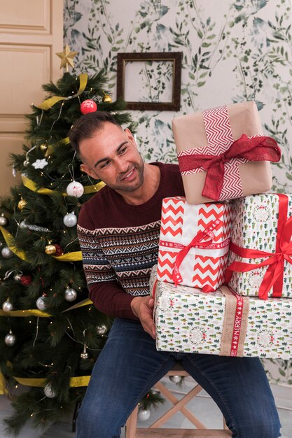 Guy with heap of gifts on chair near Christmas tree