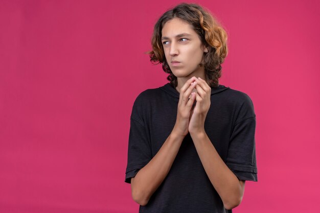 Guy with long hair in black t-shirt something hiding on pink wall