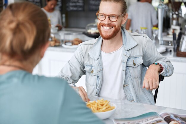 Guy with long hair, dressed in fashionable denim jacket in cafe
