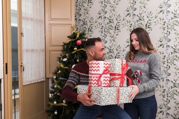 クリスマスツリーの近くに贈り物と魅力的な女性の山を持つ男