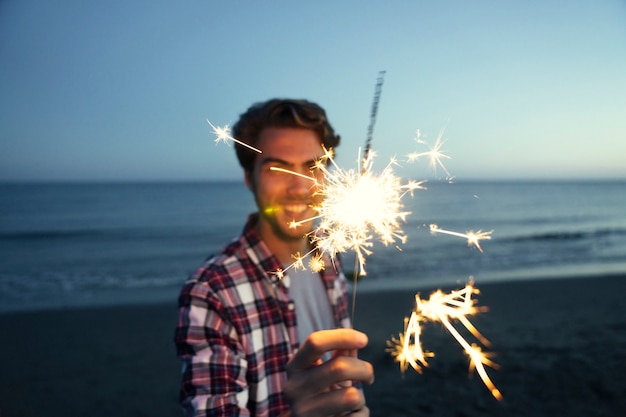 Foto gratuita guy con sparkler in una spiaggia di tramonto