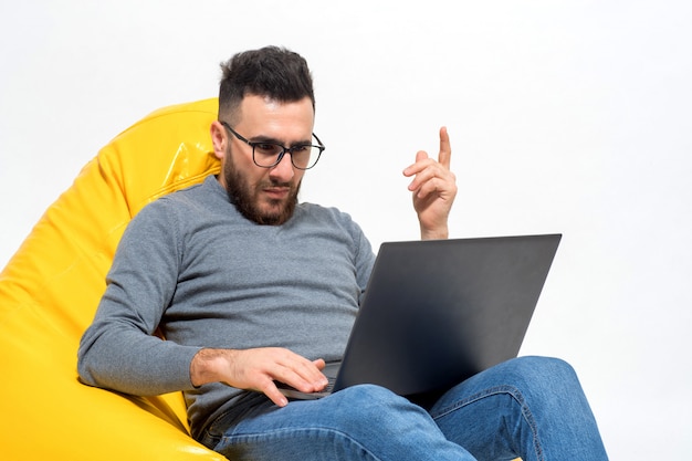 Guy lavora con il computer portatile mentre è seduto sulla sedia pouf giallo