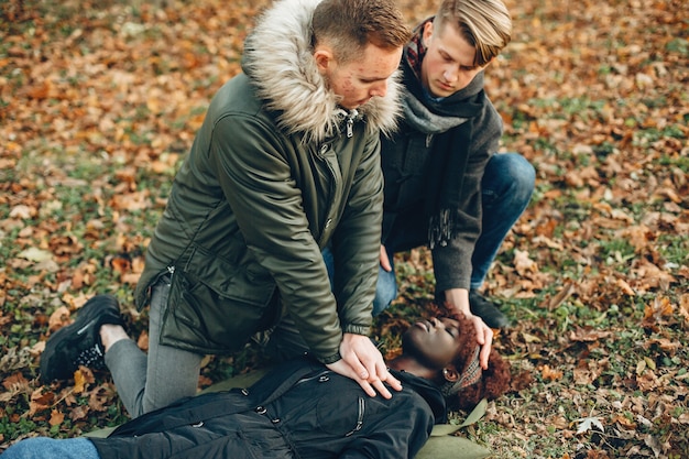 Foto gratuita i ragazzi aiutano una donna. la ragazza africana sta mentendo inconscia. fornire il primo soccorso nel parco.