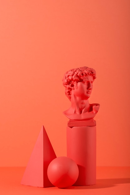 Gypsum bust on coral background with geometric shapes