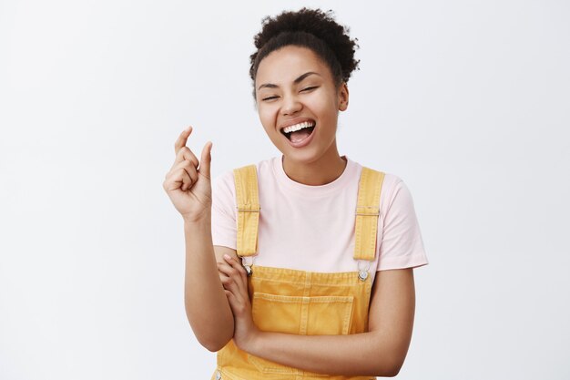 Ha-ha so small. Portrait of joyful emotive young woman with dark skin and curly hair, shaping tiny and funny object with fingers, laughing out loud, scolding someone cause of size over grey wall