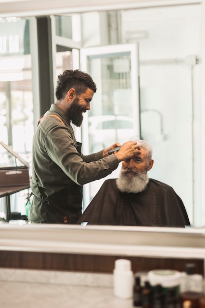 Foto gratuita capelli dello stilista che rifilano capelli al maschio invecchiato in salone