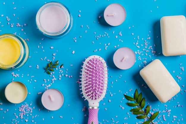 Hairbrush; soap and cream with pink salt spread on blue background