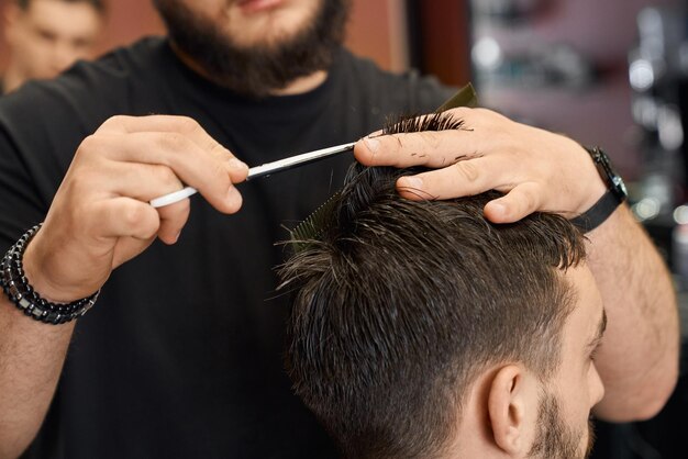 Парикмахер стрижет волосы клиента-мужчины острыми ножницами