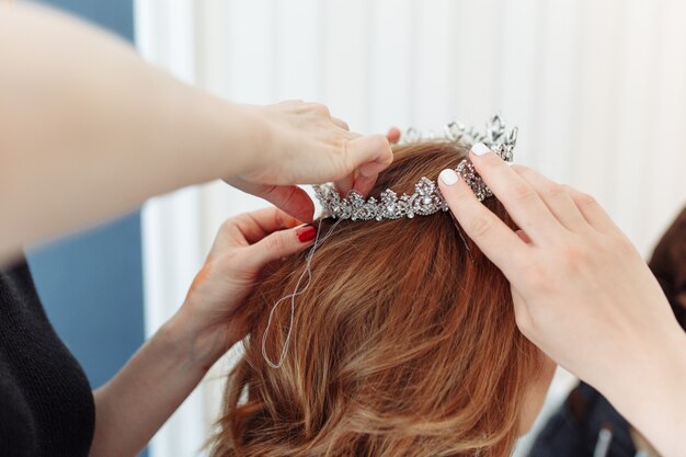 hairdresser makes models hairstyle for bride, putting on tiara crown.
