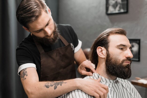 Hairdresser putting cape on male client in barber shop