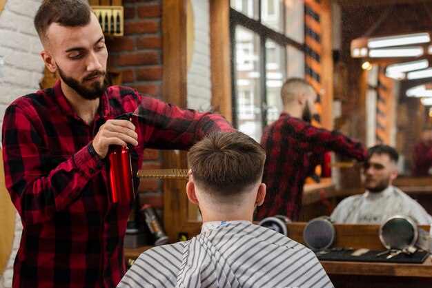 Парикмахер окропляет волосы молодого человека