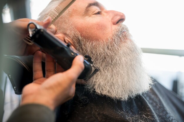 Hairdresser trimming beard to aged man