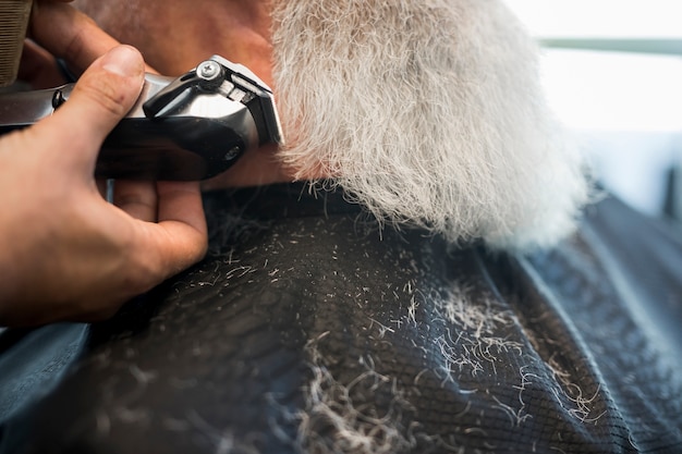 Hairdresser trimming beard with electric razor to client