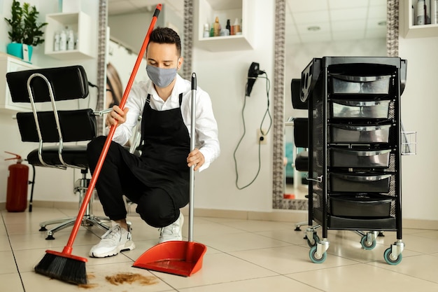 Hairdresser with protective face mask cleaning salon after a haircut