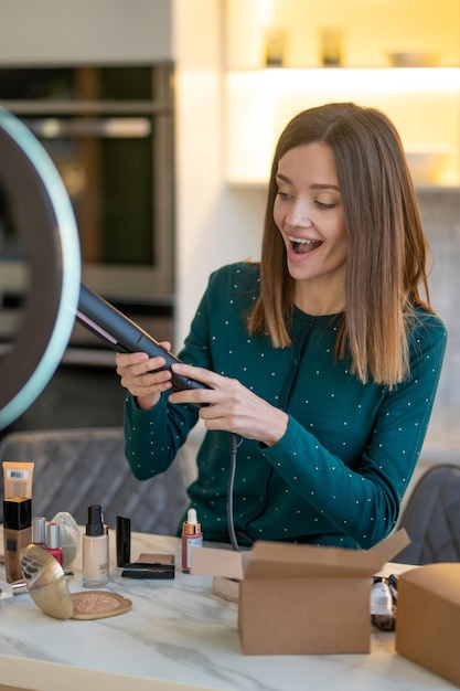 Hairdressing. Smiling young hairdresser holding hair straighntener and looking contented