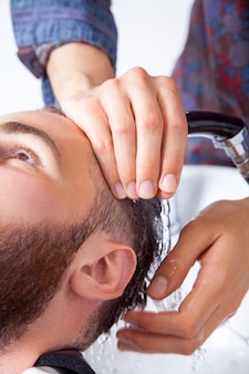 ヘア​スタイリング​。​散髪​の​準備​を​している​間​、​理髪店​で​彼​の​クライアント​の​頭​を​洗う​理髪店​の​トリミングされた​画像