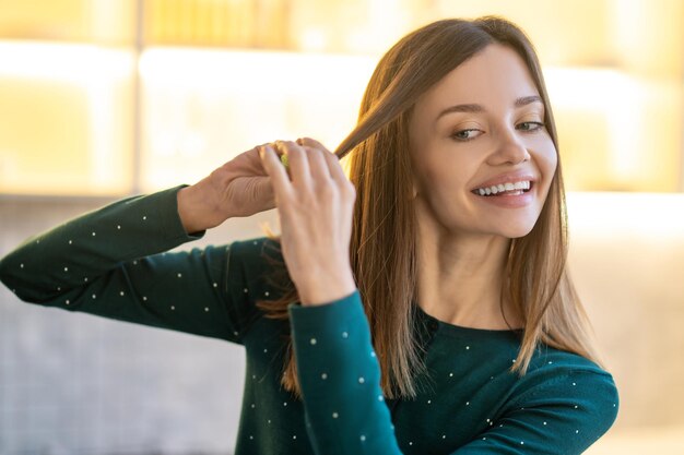 ヘアスタイリング。ヘアスタイリングのヒントを示す笑顔の若い女性