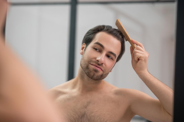 Hairstyling. Young handsome man brushing his hair and looking contented