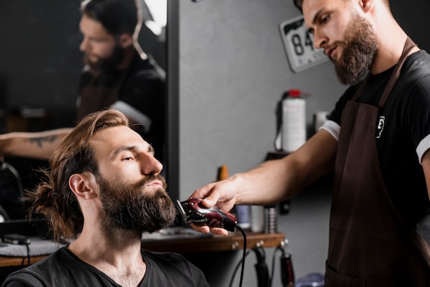 Hairstylist trimming male client's hair with electric trimmer