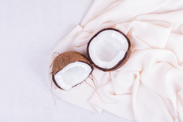 Hairy coconut broken into half on white tablecloth.