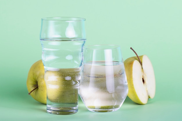 Free photo half apple and water glasses on green background