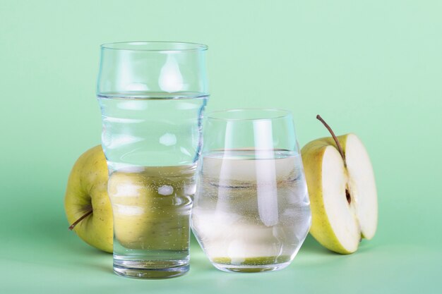 Half apple and water glasses on green background