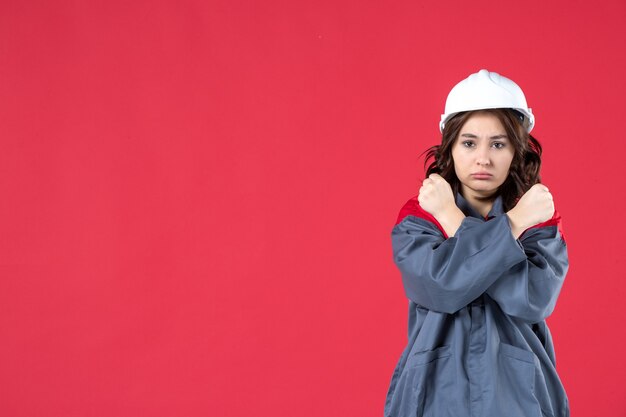 모자를 쓴 제복을 입은 화난 여성 건축업자의 반신 사진과 고립된 빨간색 배경에서 정지 제스처를 취하는 모습