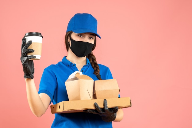 Free photo half body shot of hardworking courier girl wearing medical mask and gloves holding orders on pastel peach background