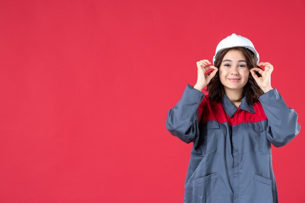 Half body shot of smiling female builder in uniform with hard hat on isolated red background