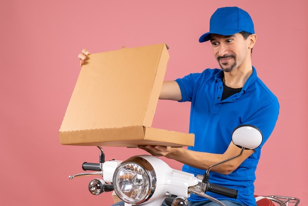 Colpo a metà corpo di un uomo sorridente che consegna il fattorino che indossa un cappello seduto sull'ordine di apertura dello scooter