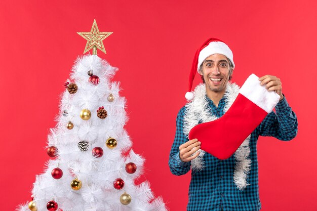 파란색 벗겨진 셔츠에 산타 클로스 모자와 크리스마스 양말을 들고 젊은 남자의 절반 바디 샷