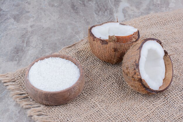 Half cut coconuts and bowl of sugar on stone background. 