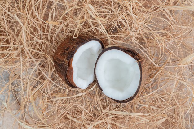 Half cut coconuts with straws on marble surface.