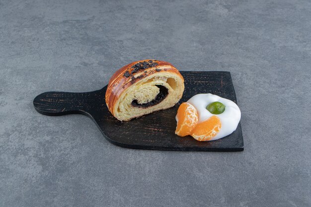 Half-cut croissant with tangerine slices on black cutting board.