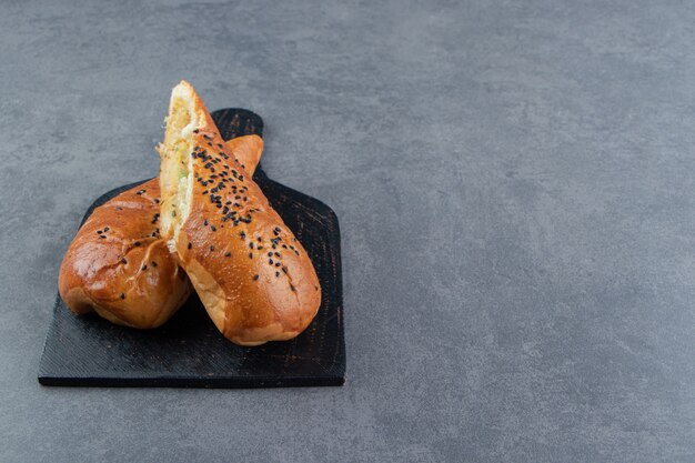 Half-cut fresh pastries with sesame seeds on black board.