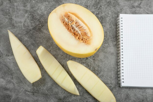 Half cut fresh sweet melon and empty notebook on marble surface. 