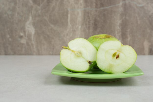 Половина нарезанных зеленых яблок на зеленой тарелке.
