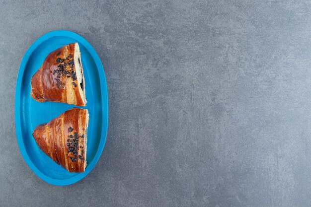 Half-cut tasty croissants with chocolate on blue plate. 