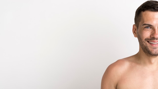 Half face of shirtless smiling young man standing against white background