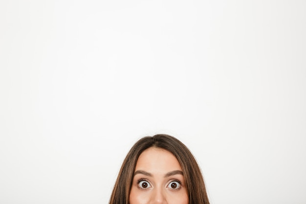 Half face of surprised brunette woman looking at the camera over grey